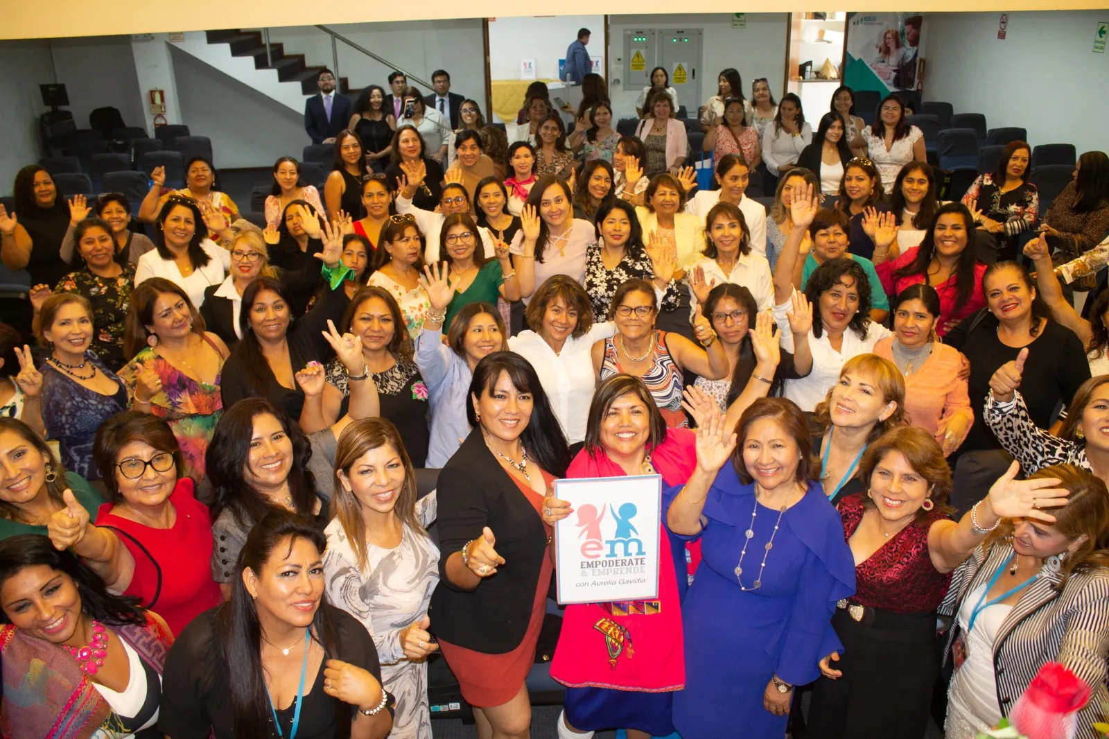 Grupo numeroso de mujeres saludando, con un cartel de Empodérate y Emprende con Aurelia Gavidia